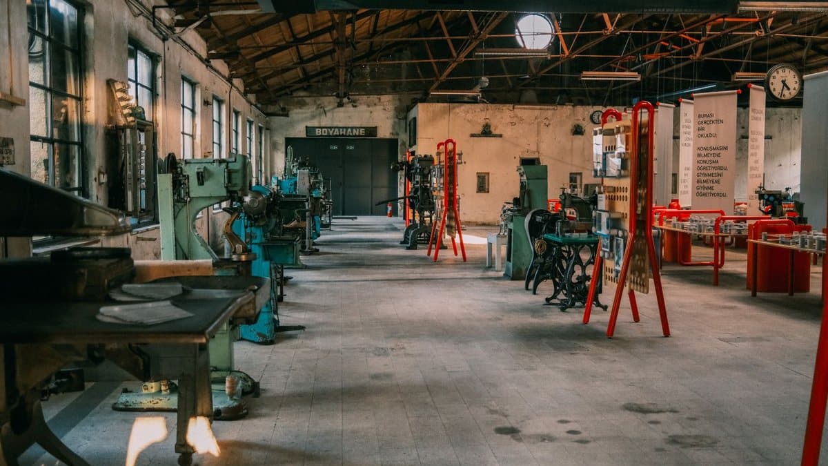 A wide industrial hall converted into an exhibition space displays vintage machinery, red stands, and information panels under a high beamed ceiling.