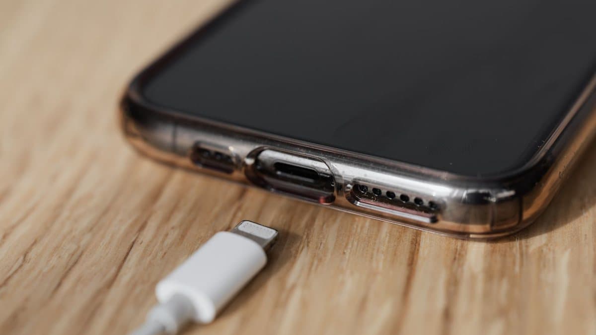 A smartphone in a clear protective case lies on a wooden surface, with a white charging cable connector nearby.