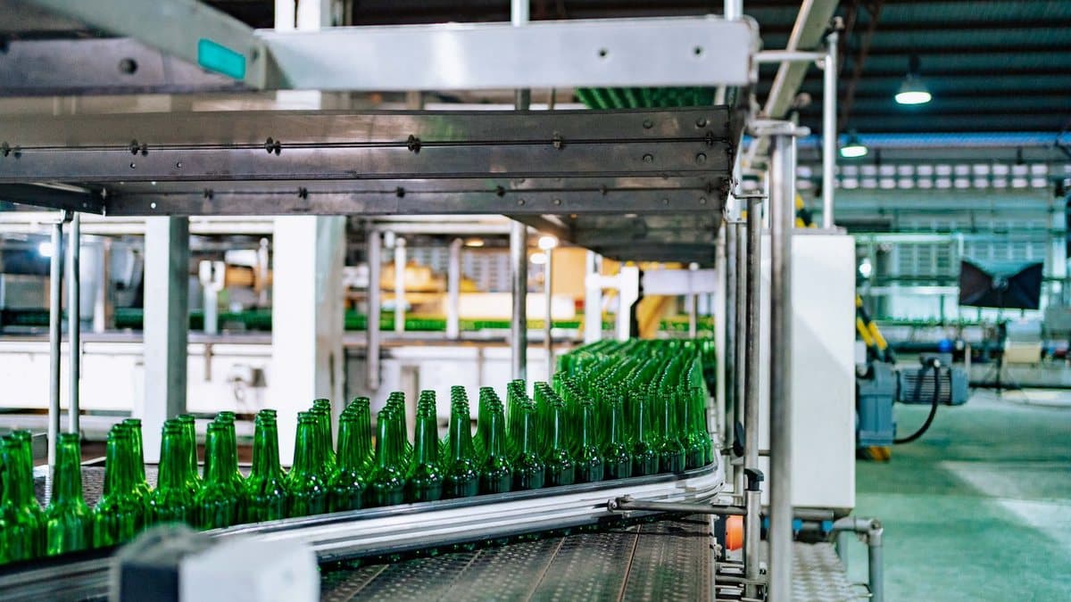 Green glass bottles move along multiple conveyor belts within an industrial facility, suggesting automated production.