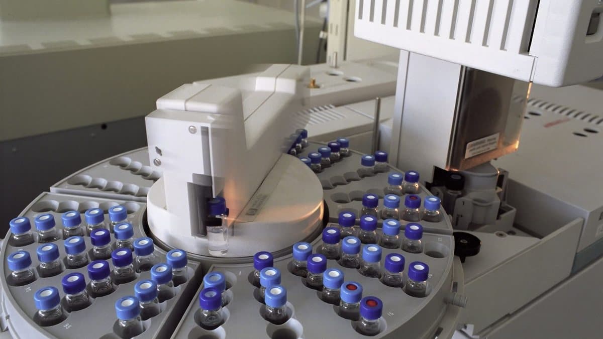 An automated laboratory instrument featuring a circular tray loaded with numerous small sample vials for analysis.