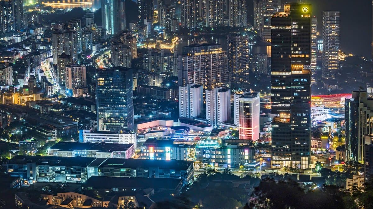夜晚,一座灯火通明的现代化城市景观,高楼林立,街道璀璨,远处可见一片水域。