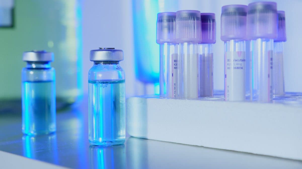 Vials with blue liquid and test tubes in a white rack are illuminated by blue and purple light in a laboratory setting.