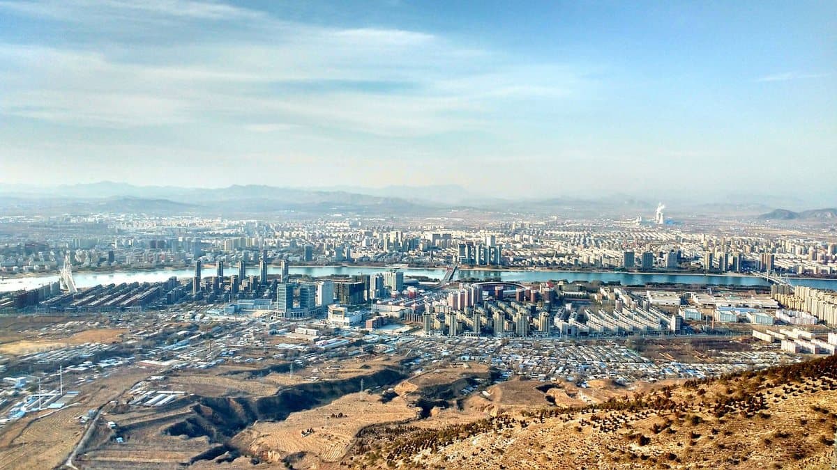 A panoramic view of a vast city with a wide river flowing through it, seen from a dry, elevated landscape.