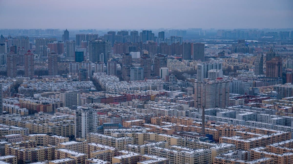Expansive aerial view of a densely packed city with countless buildings under a grey sky, many rooftops dusted with snow.