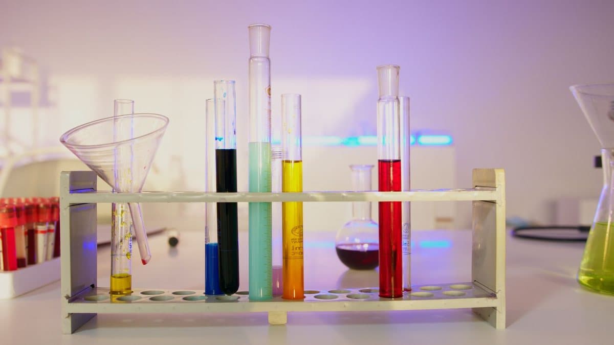 A test tube rack displays many test tubes filled with brightly colored liquids, with a funnel and other glassware nearby.