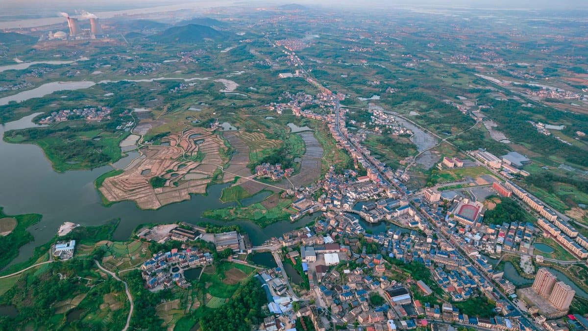 An aerial view shows a sprawling landscape of green fields, waterways, small towns, and distant power plant cooling towers.