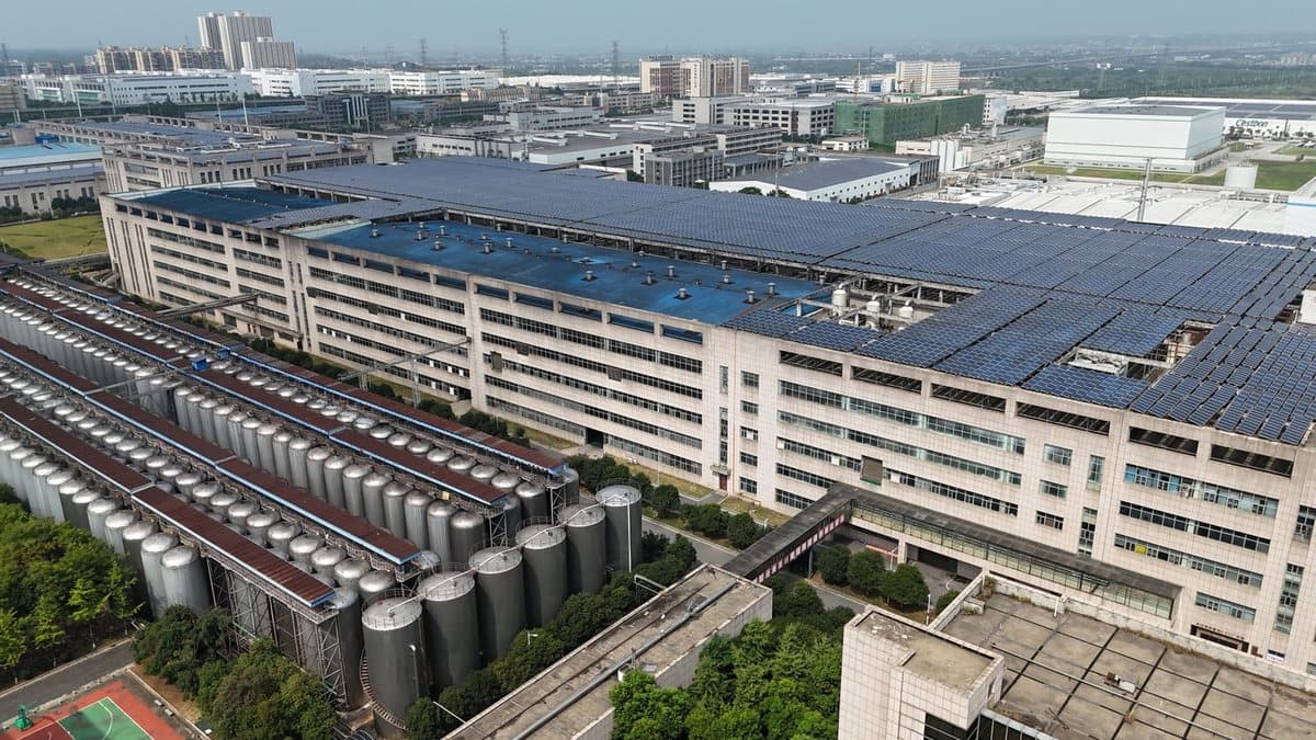 Aerial view of a large industrial complex featuring multiple buildings, extensive rooftop solar panels, and numerous storage tanks.