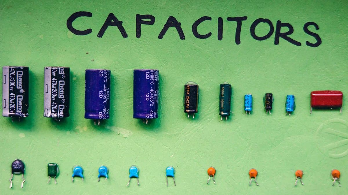 Various types and sizes of electronic capacitors are neatly arranged on a vibrant green surface, with "CAPACITORS" written above.
