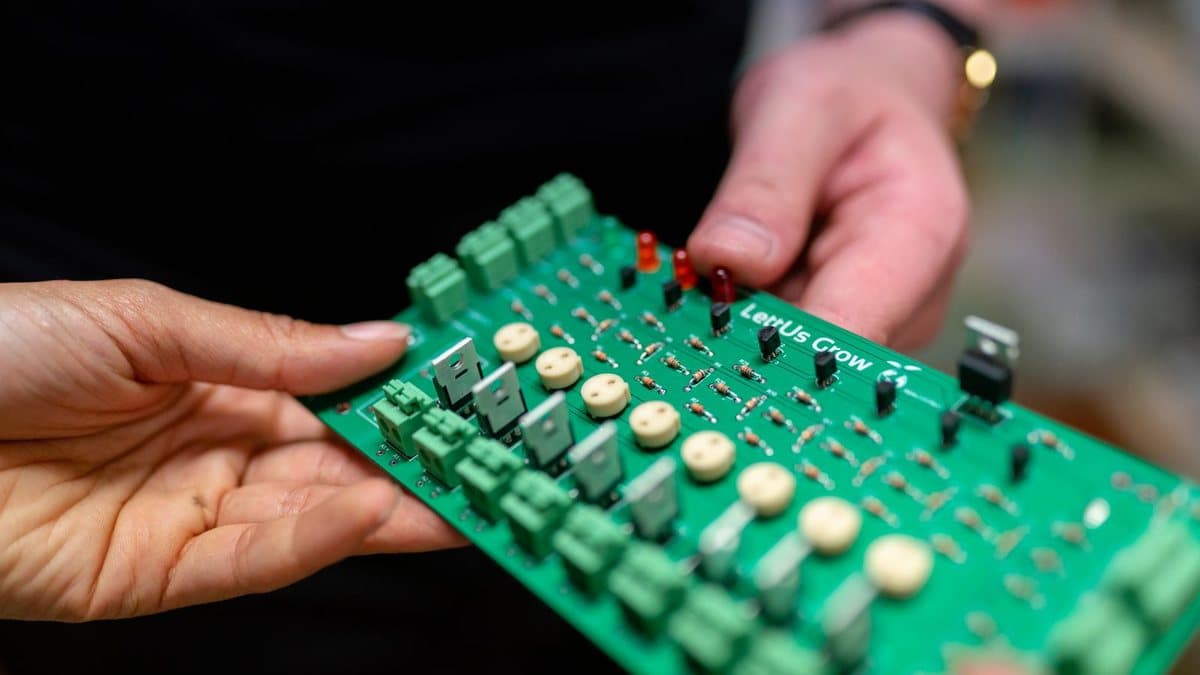 Two hands hold a green circuit board filled with various electronic components like resistors, terminals, and LEDs.