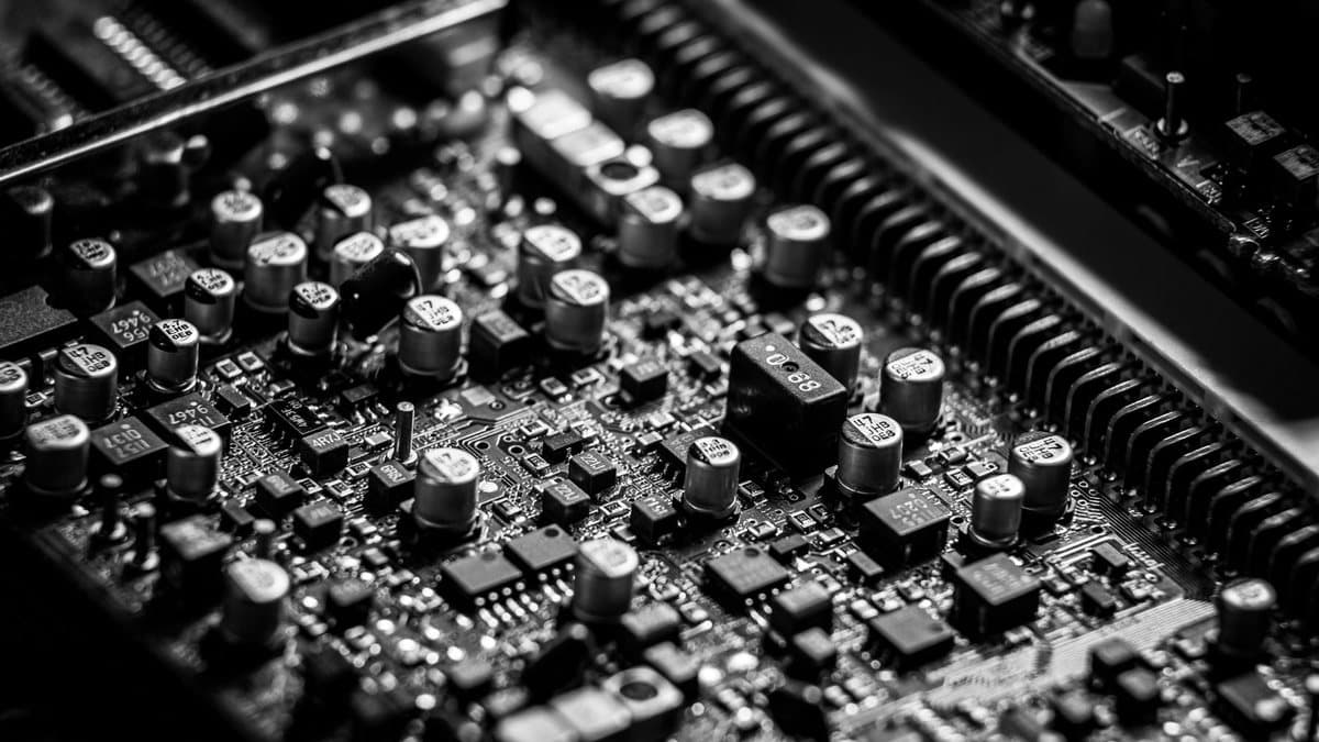 A monochromatic close-up captures the intricate details of a circuit board, featuring numerous capacitors, resistors, and integrated circuits.