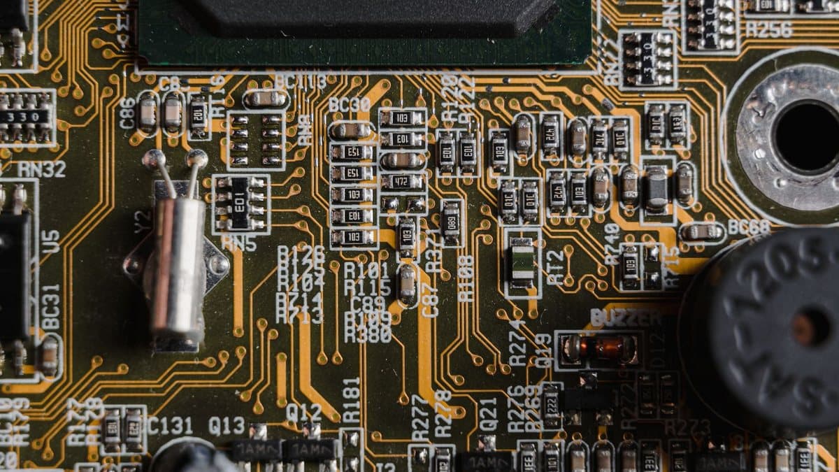 A close-up of a circuit board featuring numerous small electronic components, golden traces, and various labels on a dark green surface.