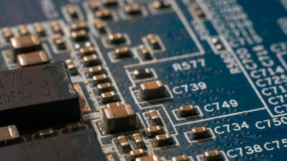 A detailed close-up of a blue circuit board densely populated with numerous tiny electronic components and identifying numbers.