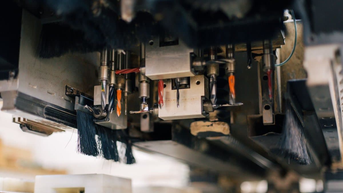Close-up of a multi-tool industrial machine showing several drill bits, some with colored flutes, and dust-collection brushes.