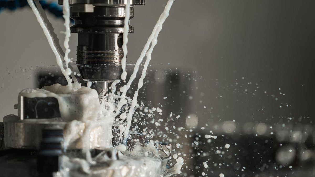 A close-up shot of a machine tool cutting a metal workpiece, with white coolant spraying and splashing around the contact point.