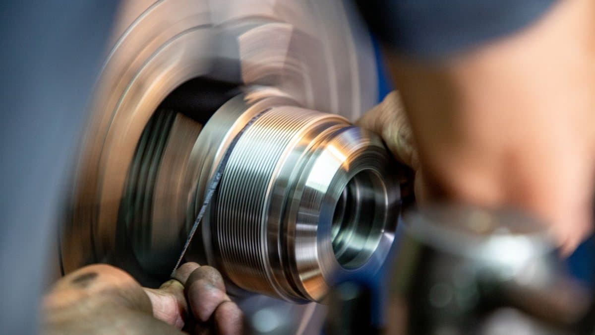 Close-up of a worker's hands using a tool on a rapidly spinning, threaded metal component.