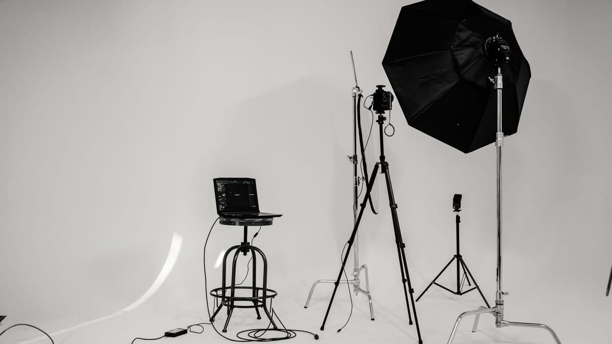 A photography studio setup: a laptop on a stool, a camera on a tripod, and a large octagonal softbox on a stand.