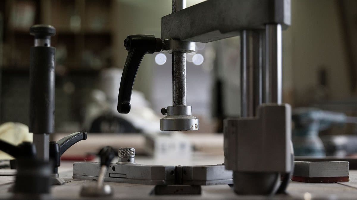 Detailed view of metal industrial equipment featuring vertical shafts, a black lever, and a base in a workshop setting.