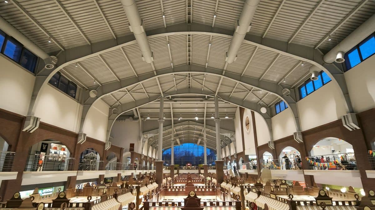 A spacious indoor hall with a high arched metal ceiling, upper windows, multi-level walkways, and rows of market stalls below.