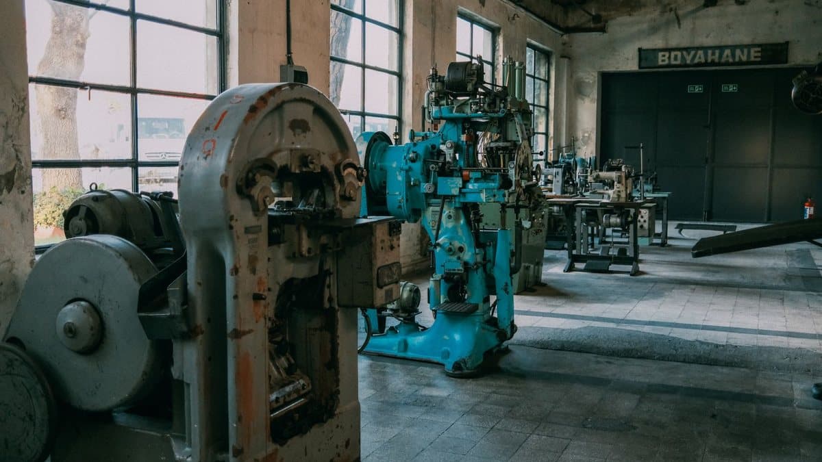 An expansive industrial workshop with large windows displays various grey and blue machinery, sewing tables, and a 'BOYAHANE' sign.