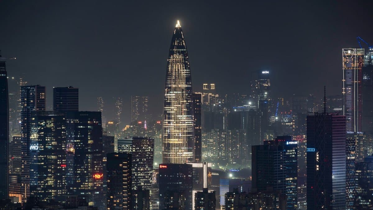 夜晚,一座明亮的尖顶摩天大楼在广阔朦胧的城市中耸立,周围环绕着无数闪烁灯光的建筑。
