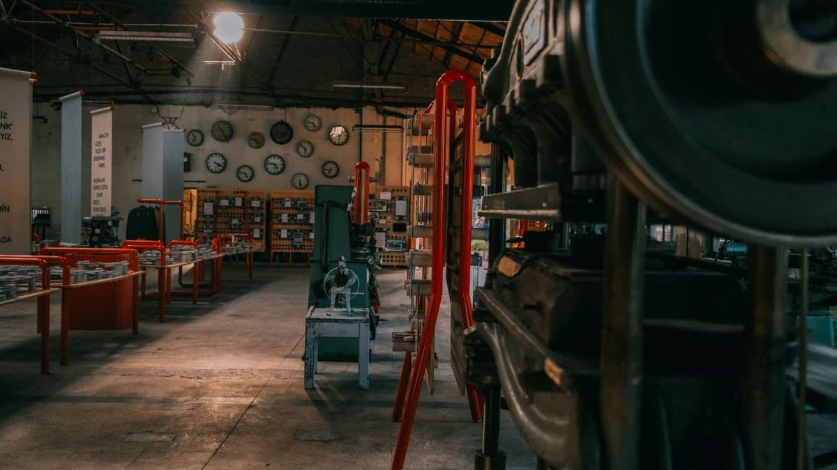 An expansive industrial-style room showcases vintage machinery, red display stands, and a wall adorned with numerous clocks.