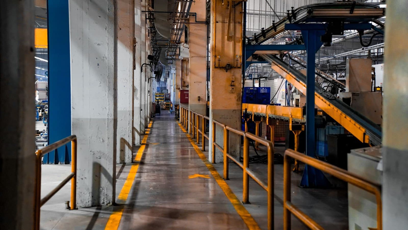A raised walkway inside a plant, running past overhead pipework and machinery under a metal roof.